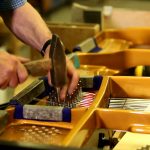 Hände, die mit dem Hammer ein Klavier zusammenhänmmern.